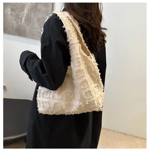Détail du sac cabas beige matelassé aux bords effilochés sur un trench-coat noir