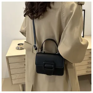 Détail d'un sac à main noir minimaliste avec boucle porté par un modèle en trench-coat