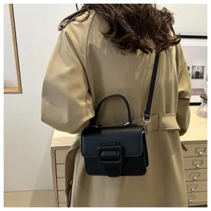 Detailed view of a black leather crossbody bag with square buckle on a trench coat