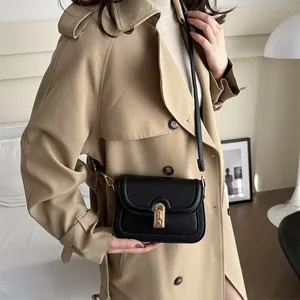 Minimalist black leather crossbody bag with golden twist lock on a khaki trench coat