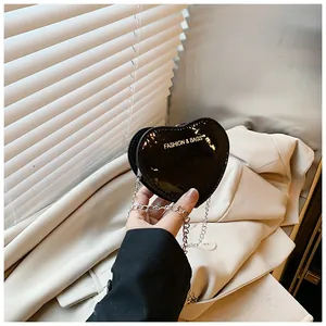 Detail of a mini black patent leather heart-shaped bag with a silver chain and logo