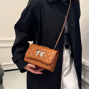 Caramel quilted crossbody bag with silver bow accent and chain strap shown on a model