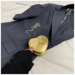 Close-up of heart-shaped mini gold mirror crossbody bag with silver chain on grey blazer