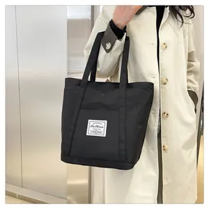 Detalle del bolso tote de nailon negro con bolsillo frontal, cierre de metal y etiqueta tejida