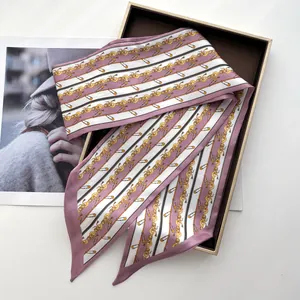 Detail view of a long narrow silk scarf with elegant gold chain print and pink twill