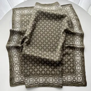 Macro detail of olive green silk scarf featuring white geometric patterns and ethnic border