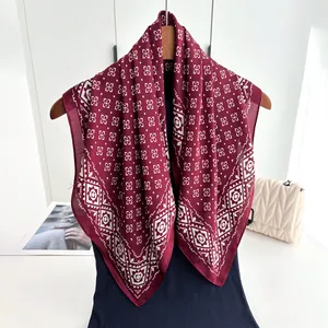 Detail view of burgundy floral geometric print silk scarf draped on a wooden hanger
