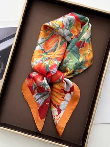 Detailed close-up of silk-like scarf with vibrant orange flower print in gift tray