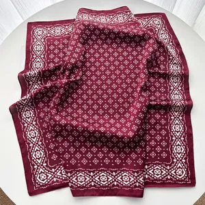 Detailed view of the soft silk-like texture and geometric floral pattern on a burgundy scarf