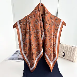 Detail of rust red paisley silk scarf with white border hanging on a wooden hanger