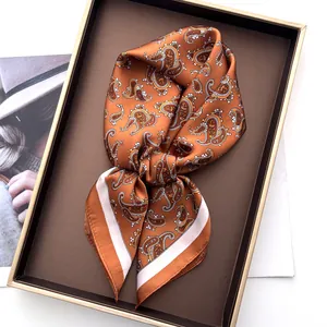 Detail of folded paisley silk scarf in caramel brown inside a premium gift box