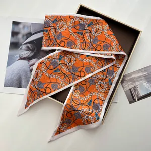 Detailed macro of orange silk twilly scarf with chain patterns on high-end gift box