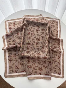 Detail of silk-like square scarf featuring beige paisley patterns and geometric borders