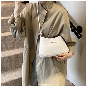 Detail of white V-textured shoulder bag with gold hardware worn over a khaki trench coat