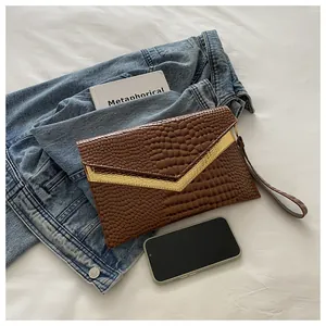 Detailed view of dark brown croc-pattern envelope clutch with gold V-shape metal trim