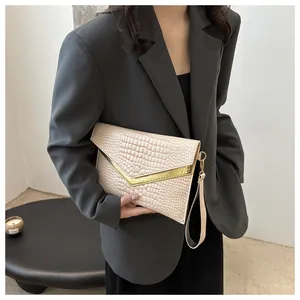 Detailed view of beige crocodile embossed clutch with V-shaped gold metal trim and wristlet