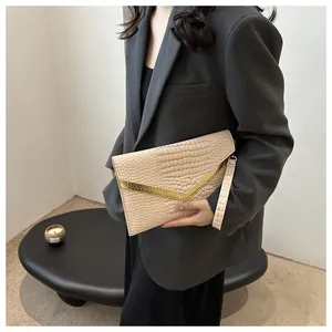 Detail of beige crocodile pattern envelope clutch with gold metal V-trim and wristlet
