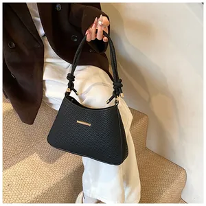 Detail of black textured underarm bag with gold metal buckle and woven handle