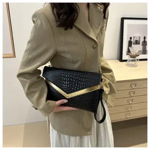 Detail of black crocodile pattern envelope clutch with golden V-shaped metal trim