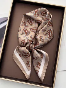 Detailed close-up of champagne silk square scarf featuring orange paisley prints on a leather tray