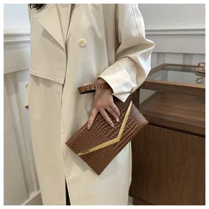 Detail of a brown crocodile pattern envelope clutch bag held by a model in a trench coat