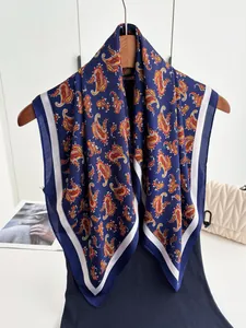 Detail of navy blue silk-like square scarf with intricate orange paisley patterns on a hanger