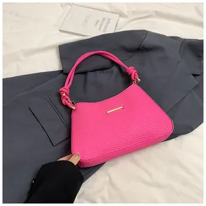 Detail of neon pink underarm bag featuring a knotted rope handle and gold metal trim