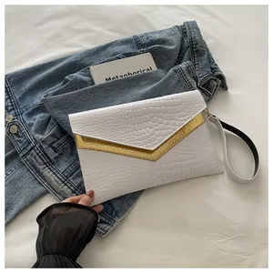 Detail of white crocodile pattern envelope clutch with gold V-shaped metal trim on denim