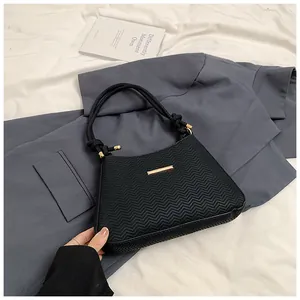 Detail of black underarm bag featuring wave texture, golden bar clasp and woven strap