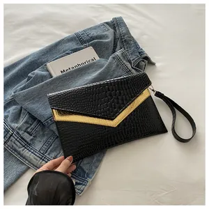 Detail of black crocodile texture envelope clutch with gold metal V-shaped trim