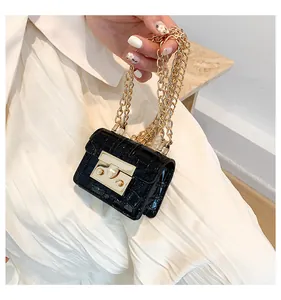 Close-up of black stone pattern mini bag with gold chain held by a person over white fabric