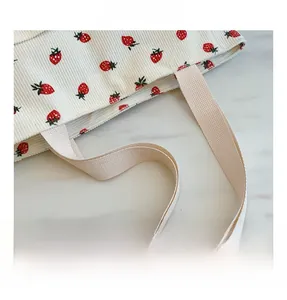 Detailed macro view of strawberry print on corduroy tote bag with woven handle