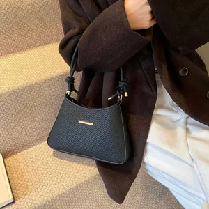 Black underarm bag with herringbone texture and gold buckle on a stylish model