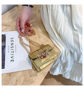 Close-up of golden crocodile pattern mini chain bag with metallic lock on wooden surface