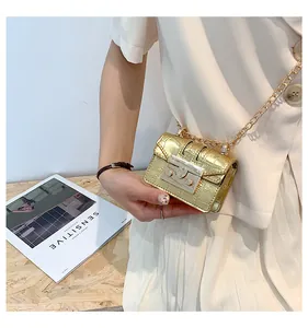 Detail of a mini gold crocodile embossed chain bag worn by a model in casual attire