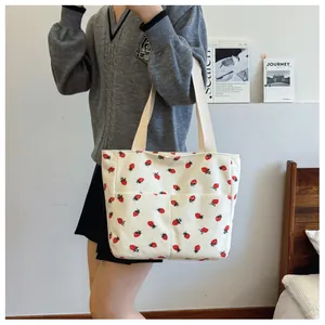 Close-up of cream corduroy tote bag featuring red strawberry prints and functional front pockets