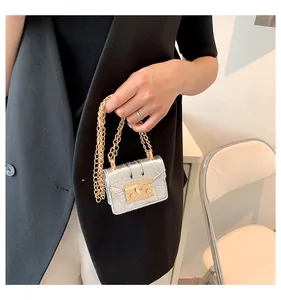 Macro detail of silver crocodile pattern mini bag with golden metal buckle and chain strap