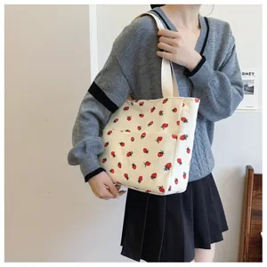 Detail of strawberry print corduroy tote bag showing side pocket and woven strap
