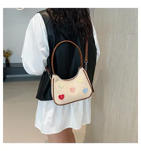 Dettaglio della borsa in tela con toppe a cuore e finiture in pelle marrone su modella