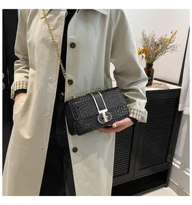 Detail of black crocodile texture handbag with gold chain strap and metal lock closure