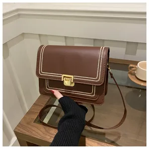 Detail of vintage brown crossbody bag with gold press lock and white decorative stitching