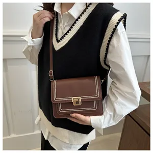 Detail of a brown leather crossbody bag with white stitching and a golden square lock