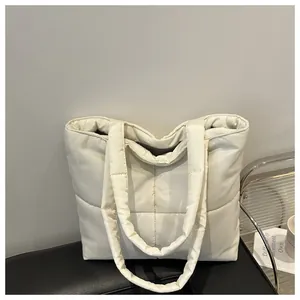 Close-up of quilted nylon tote bag in off-white finish on a black leather stool