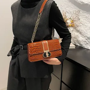 Brown crocodile pattern crossbody bag with gold lock and chain strap on shoulder