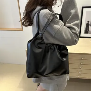 Minimalist black pleated cloud tote bag in soft PU leather worn over the shoulder