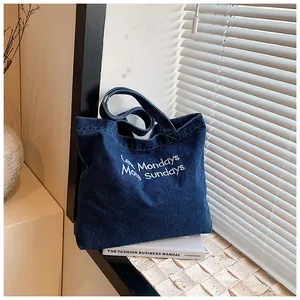 Detail of white embroidery and sturdy stitching on dark blue denim canvas tote bag