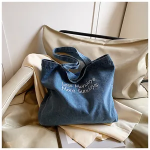 Detail of the blue denim tote bag featuring white Less Mondays More Sundays embroidery