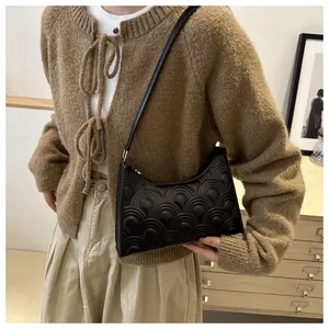 Detail of black scalloped quilted underarm bag worn with a vintage knit cardigan