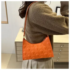 Detail of a bright orange underarm bag featuring a 3D semi-circular embossed texture pattern