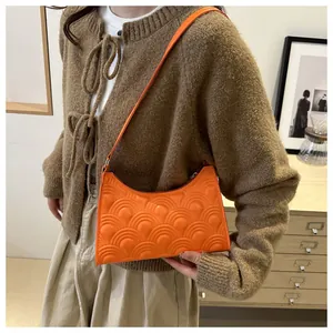 Detail of orange embossed leather underarm bag worn with a brown knit cardigan